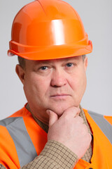 middle-aged construction worker in helmet with hand under chin looking at camera, head of successful plump engineer