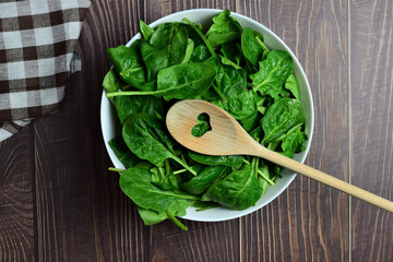 Fresh spinach leaves in a white bowl. Rustic wooden boards and copy space.