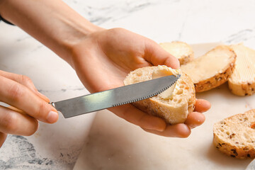 Woman spreading butter onto slice of bread on light background, closeup