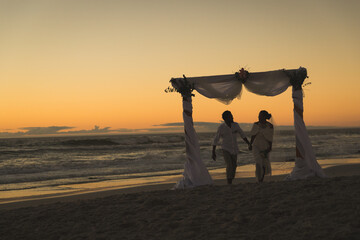 African american couple in love getting married, walking on beach during sunset holding hands