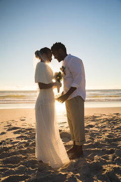 African american couple in love getting married on beach touching foreheads