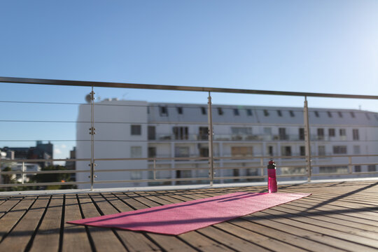 Yoga mat and water bottle on sunny wooden deck of city roof terrace