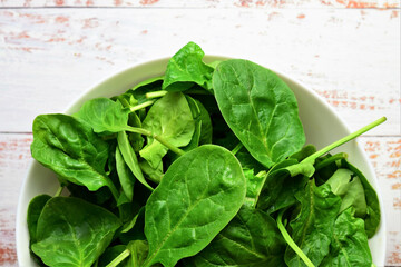 Healthy food, vegetables, fresh spinach leaves in a large white bowl. Zenith view and copy space.