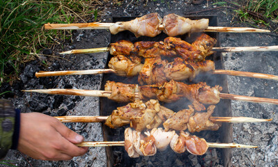 Top view of cooking shish kebab on wooden sharp homemade ecological skewers in the grill. The hand is out of focus. Picnic in nature. A lot of gray soot.