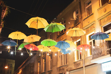 Fototapeta na wymiar Many colorful umbrellas hang on the city streets at night.