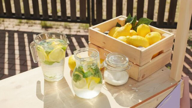 High-angle shot of diy wooden stand with box of fresh lemons and glass decanters with homemade lemonade on sunny summer day
