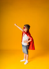 little boy toddler in a hero costume with a red mask and cape on a yellow background with space for text