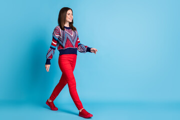 Full length body size photo of girl in red pants knitted sweater walking forward smiling isolated vivid blue color background copyspace