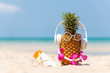 Summer in the party.  Hipster Pineapple Fashion in sunglass and listen music with sunblock and sandal on the sand beach beautiful blue sky background.  Creative art fruit for tropical style