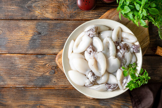 Raw cuttlefish in a ceramic plate on the kitchen table. Lots of peeled squid in a bowl on a brown wooden table top view. The concept of cooking shellfish