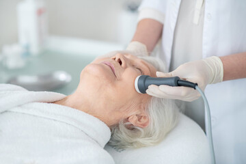 Beautician doing microcurrents therapy to an elderly customer