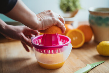 Woman squeezing orange to make orange juice in the morning (side view).