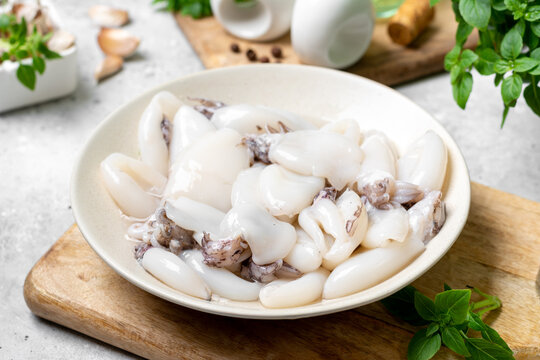 Raw cuttlefish in a ceramic plate on the kitchen table. Lots of peeled squid in a bowl on a light background. The concept of cooking shellfish