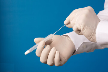 Doctor hands with hyssop and transport vial, process for coronavirus analysis, blue background.