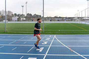 Fototapeta premium Hard working young runner boy doing warm-up in blue running track.