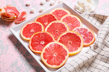 Fototapeta na wymiar Plate with slices of ripe grapefruit and sugar on color background