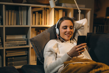 young woman relaxing on sofa at her home. she is listening to a music on headphones