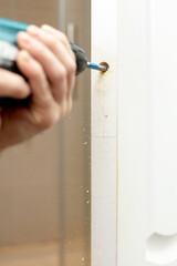 Male hands use an electric drill to drill a hole in the door. 