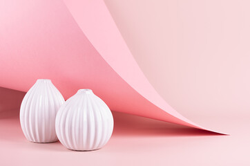 Delicate spring pink interior with ribbed white ceramic vases on soft light pastel background with hovering curved paper, peak. Fashion simple minimalist style.