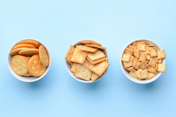 Bowls of crackers on color background