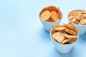 Bowls of crackers on color background
