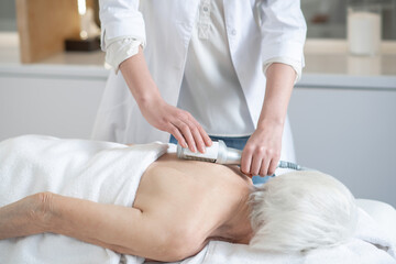 Massage therapist doing back massage procedures to a gray-haired woman