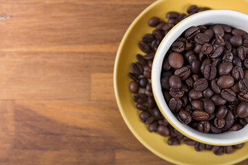 coffee cup top view, yellow ceramic cup and saucer filled with coffee beans on a wooden surface, with space to write to the left, horizontal photo