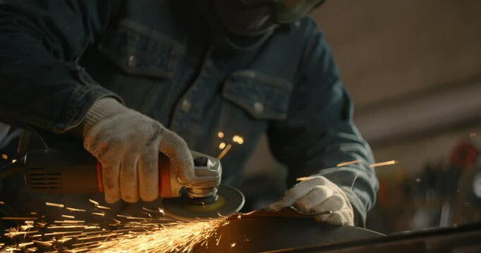 Locksmith sands the edges of a metal detail by electric grinder with a lot of sparks in slow motion, metalwork at workshop, 4k 60p Prores HQ