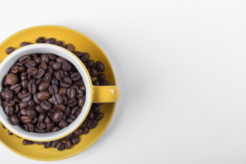 coffee cup top view, yellow ceramic half cup filled with coffee beans on a white surface with space for writing on the right, horizontal photo