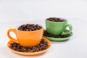 set of two ceramic cups with their plates one orange and one green filled with coffee beans, on white background, horizontal photo