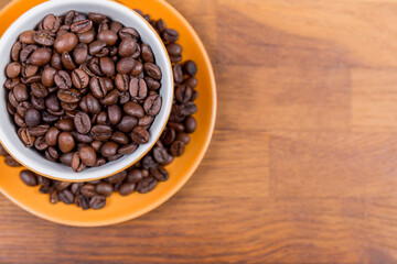 coffee cup top view, orange ceramic cup and saucer filled with coffee beans on a wooden surface, with space to write to the right, horizontal photo