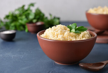 Bowl with tasty couscous and parsley on dark background