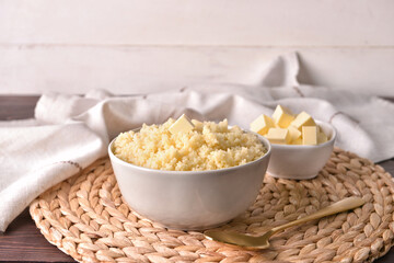Bowls with tasty couscous and butter on light wooden background