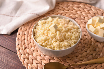 Bowls with tasty couscous and butter on wooden background