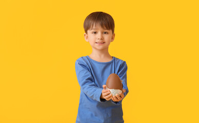 Cute little boy with chocolate Easter egg on color background