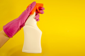 A female hand in a pink glove holds a white spray on a yellow background. Cleaning concept with copy space