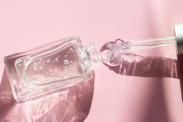 Glass bottle with fluid collagen and hyaluronic acid, hydration skin with shadows on pastel pink background on sunlight. Cosmetology, dermatology concept. Top view, flat lay, copy space., soft focus.