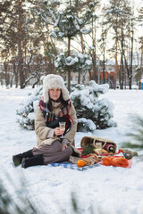 Girl on Romantic picnic in winter park, color blanket. Fresh food, cheese, oranges, croissants, wine and walnuts. Outdoor relaxing, fresh air eating