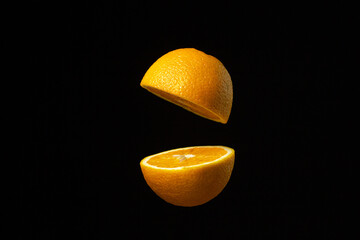Orange cut in half in the air against a dark background. Sliced orange on a black background....