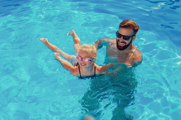 Father teaching baby girl to swim in the pool