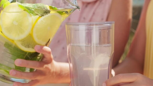 Midsection close up of unrecognizable girls pouring homemade lemonade in glass on hot summer day