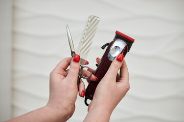 Close-up picture of hairdresser's tools in female hands isolated on white background. Professional trimmer, comb and scissors for perfect haircut by hair stylist. Work process in barber shop.