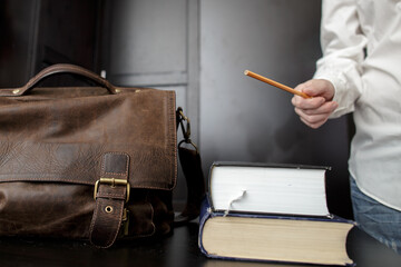 Brown leather briefcase and a stack of books on the teacher's desk, who is standing nearby and explaining something.