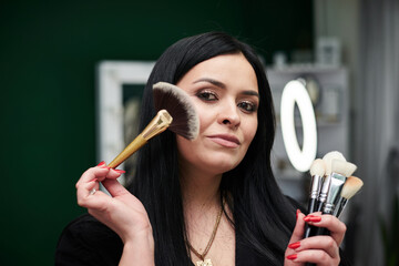 Portrait of make-up artist at workplace in beauty studio, holding various brushes and palette. Work process in beauty salon. Getting ready for gala dinner with help of professional stylist.