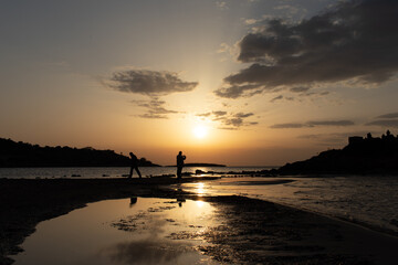 People's silhouette walking at the beach with the sunset at background