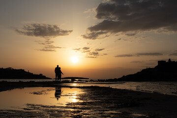 Fototapeta premium People's silhouette walking at the beach with the sunset at background