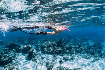 Woman with fins swimming in transparent ocean.