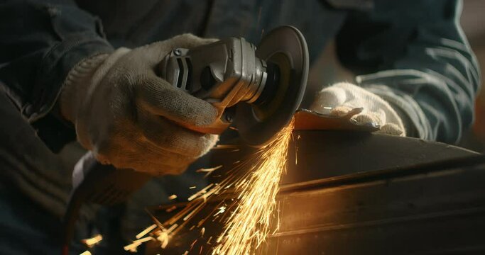 Locksmith sands the edges of a metal detail by electric grinder with a lot of sparks in slow motion, metalwork at workshop, 4k 60p Prores HQ