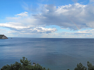 Seascape blue sea and rainbow on a bright sky with white clouds on a summer day after rain