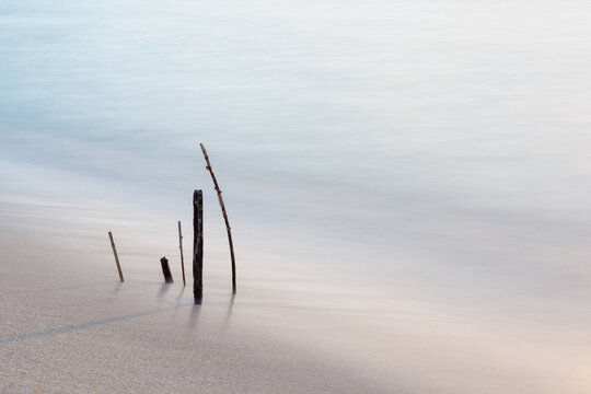 Fototapeta long exposure of wooden sticks sticking out of the water on the beach
